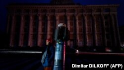 O femeie, în piața întunecată din fața clădirii avariate a Administrației Regionale de Stat din Harkov, pe 5 noiembrie 2022, după ce rachetele ruse au lovit rețelele de electricitate