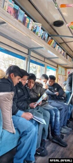 شماری از کودکان حین مطالعه کتاب در کتابخانه سیار چهارمغز