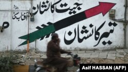 Un bărbat pe motocicletă trece pe lângă un zid pictat cu logo-ul Partidului Popular Pakistanez (PPP) pe o stradă din Karachi, 12 ianuarie 2024.