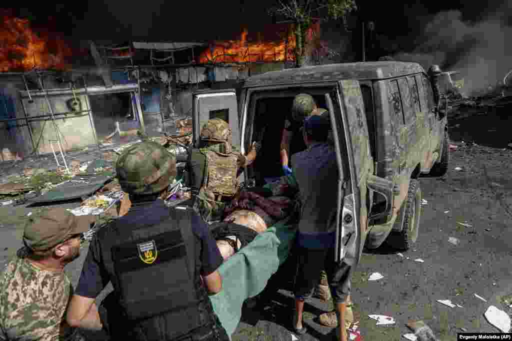 Раненого мужчину закатывают на носилках в карету скорой помощи. Рядом продолжается пожар&nbsp;