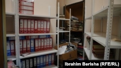 Një zyrë e vogël ku ruhen disa libra me të dhënat e pacientëve dhe disa folderë me shënime.