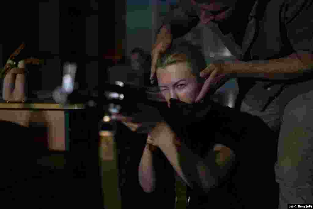 Un instructor corectează postura unei femei care ține un pistol mitralieră AK-47 în timpul antrenamentului cu arme de foc. &bdquo;Scopul principal este ca oamenii să învețe cum să supraviețuiască și cum să răspundă la aceste amenințări militare care există&rdquo;, explică Șcerbina. Prin educarea oamenilor, autoritățile locale speră să reducă, pe viitor, numărul victimelor.