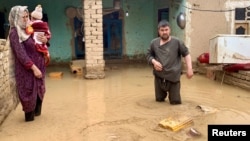 An Afghan woman holds her child as a man salvages his belongings from floodwaters outside their house in Maymana, the capital of northern Faryab Province, in May.