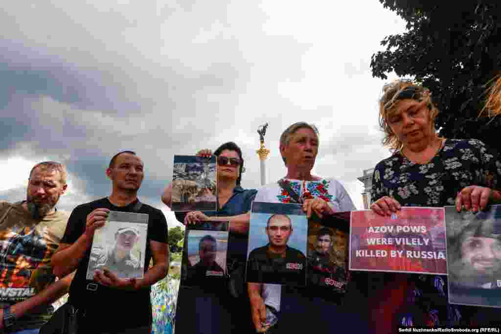 Поруч із фотографією військового жінка тримає плакат із написом: &laquo;Полонені азовці були підступно вбиті Росією&raquo; (переклад з англійської)