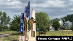 Intrarea în comuna Plenița e simbolică. Are stegurile României, ale Uniunii Europene, o troiță și pe fundal un depozit de cereale.
