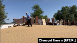 A wall devised to block the sand and a house barely visible beneath.