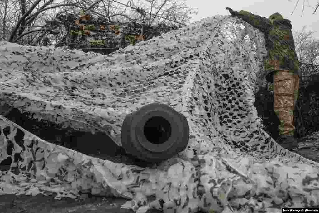 A soldier adjusts the camouflage above a 2S1 Gvozdika self-propelled howitzer. &nbsp;