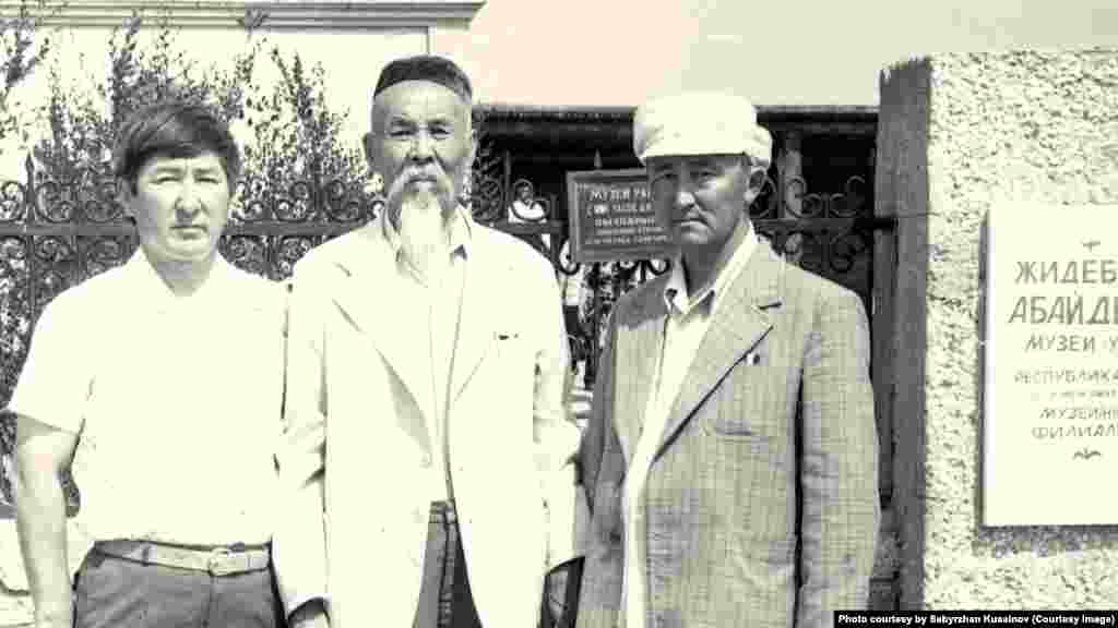 Ахат Шәкерімұлы (ортада) және "Абай" совхозының директоры Санақбек Қасымжанов (оң жақта) Жидебайдағы Абай мұражайы алдында тұр. Бұрынғы Семей облысы Абай ауданы. Сабыржан Құсайыновтың жеке архивіндегі фото.