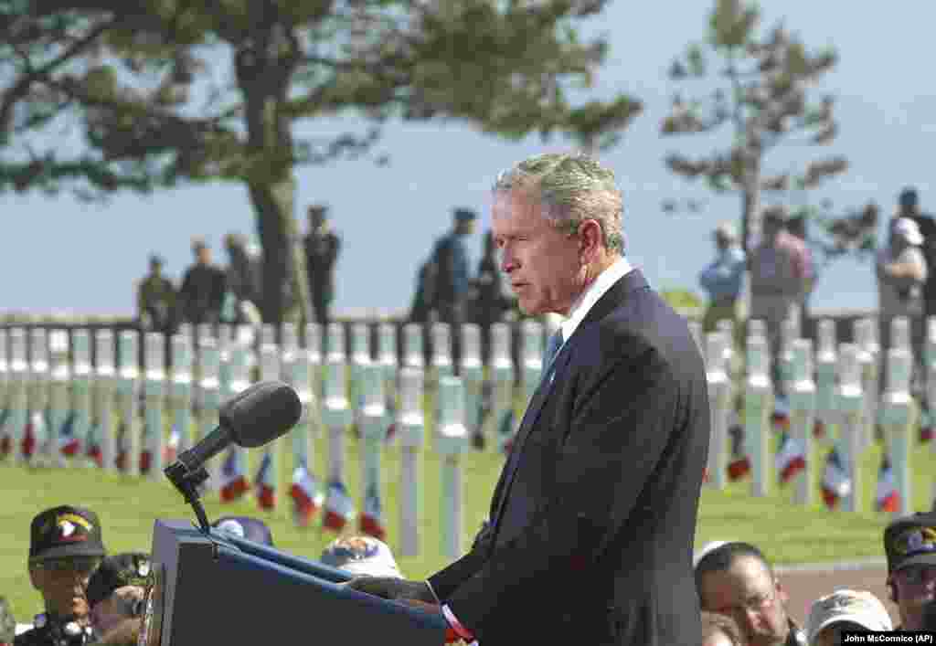 Президент США Джордж Буш виголошує промову на військовому цвинтарі в Нормандії, де похоронені американські солдати. 60-а річниця Дня висадки союзників у Нормандії. 6 червня 2004 року Тоді вперше запросили на церемонію президента Росії Володимира Путіна, який під час виступу наголосив на жертвах Радянського Союзу у війні проти німецького нацизму