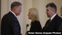 Președintele Klaus Iohannis dă mâna cu liderul PSD, Marcel Ciolacu. În fundal se vede președintele interimar al Senatului și fost lider PNL, Alina Gorghiu.