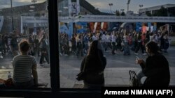 Disa gra në një stacion autobusi ndërsa në rrugë njerëzit marshojnë gjatë një proteste në Prishtinë, më 15 prill 2024, pas vrasjes së një gruaje 21-vjeçare. 