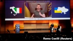 Прем’єр-міністри України та Італії – Денис Шмигаль і Джорджа Мелоні – слухають виступ президента України Володимира Зеленського (на екрані) під час Конференції з відновлення України. Рим, 26 квітня 2023 року