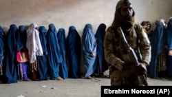 A Taliban fighter stands guard as women wait to receive food rations distributed by a humanitarian aid group in Kabul on May 23.
