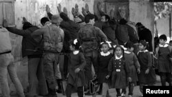 პალესტინელი სკოლის მოსწავლეები სახლში ბრუნდებიან გაკვეთილებიდან. ფონზე ისრაელის ჯარისკაცების არაბ მამაკაცებს ჩხრეკენ, მას შემდეგ რაც ებრაელი მამაკაცი მძიმედ დაჭრეს, 1986 წელი. 1987 წელს მასობრივი აჯანყება მოხდა, რომელიც ცნობილია როგორც „ინტიფადა“.