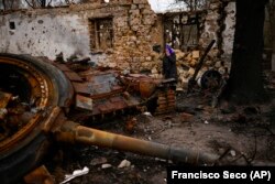 O femeie stă lângă un tanc rusesc distrus. Imagine din nordul Ucrainei, orașul Cernigău, 23 aprilie 2022. AP Photo/Francisco Seco