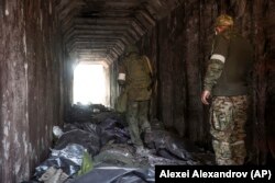 Soldați ai miliției Republicii Populare Donețk se uită la cadavrele unor soldați ucraineni în saci de plastic într-un tunel, parte a Uzinei Metalurgice Illich Iron & Steel Works, a doua cea mai mare întreprindere metalurgică din Ucraina, într-o zonă controlată de forțele separatiste susținute de Rusia în Mariupol, 18 aprilie 2022.