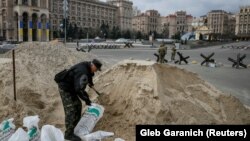 კიეველი კაცი ქვიშას ყრის ტომრებში - შორს მოჩანს ტერიტორიული დაცვის ძალების მოხალისე გუშაგები. 7 მარტი, კიევი.