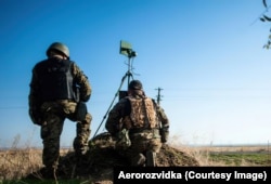 Украинские военные на учениях с беспилотниками незадолго до вторжения России в 2022 году. Мужчины просматривают экран, показывающий видео с коптера в реальном времени. Установленный на треноге передатчик поддерживает связь с дроном