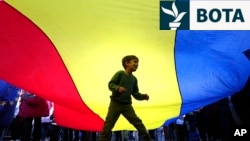 Një fëmijë luan poshtë një flamuri gjigant të Rumanisë, gjatë një eventi elektoral në mbështetje të kandidatit për president, Nicusor Dan, në Bukuresht më 11 maj.
