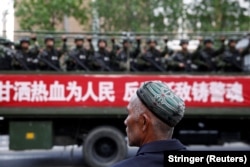 A Uyghur man looks on as a truck carrying paramilitary policemen travels along a street during an antiterrorism oath-taking rally in Urumqi, Xinjiang Uighur Autonomous Region, in 2014.