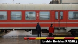 Dy persona qëndrojnë pranë një treni në Fushë Kosovë. 