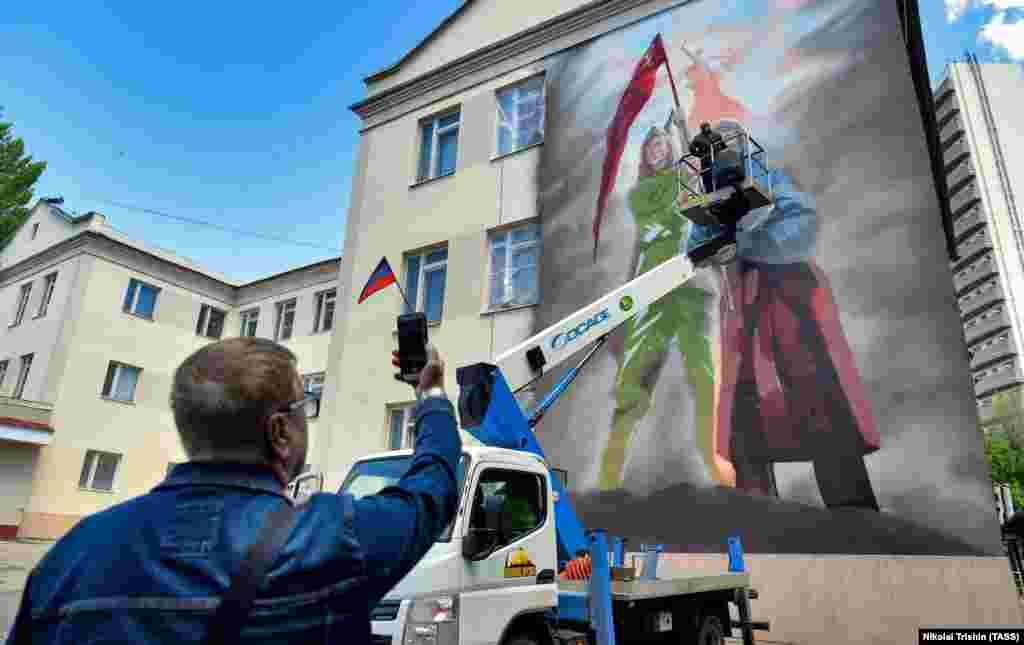 Un pictor lucrează la o pictură murală ce face trimitere la al Doilea Război Mondial și invazia Rusiei în orașul Donetsk, ocupat de Rusia în estul Ucrainei, mai 2022.