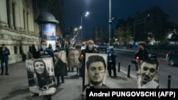 Oamenii afișează fotografii cu victimele incendiului din clubul Colectiv, în timpul unui marș comemorativ din 30 octombrie 2021, în București, România.