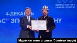"Жаратман манасчы" сынагынын жеңүүчүсү Рысбай Исаковго Мамлекеттик катчы, жазуучу Арслан Койчиев сыйлык тапшырган учур. 4-декабрь, 2025-жыл