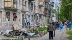 Localnici din Harkov, al doilea oraș ca mărime din Ucraina, trec pe lângă o clădire rezidențială avariată de un bombardament rusesc. Fotografie din 25 mai 2022. 