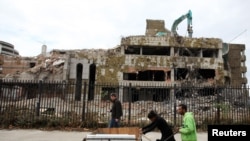 Ljudi guraju kolica kod ostataka kineske ambasade prilikom njenog rušenja u Beogradu 2010.