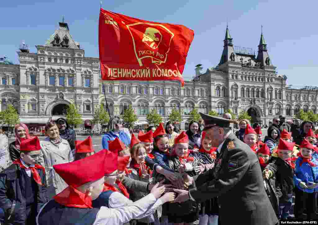 An unnamed war veteran greets children on Red Square under a flag of Lenin.&nbsp; Russian commentator Fyodor Krasheninnikov told RFE/RL's Russian Service that the purpose of Soviet-era youth movements was to make sure "young people had as little free time as possible that was not controlled by the state."