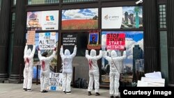 Люди в белых рабочих костюмах с красной краской на спине держат транспаранты перед зданием посольства Казахстана. Лондон, 23 января 2022 года