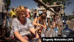 Жени полнат шишиња со вода обезбедена од волонтерска организација во Миколајев.