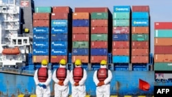 Angajați purtând echipamente de protecție personală (PPE) privesc o navă de marfă într-un port din Qingdao, în provincia chineză Shandong, la 14 ianuarie 2022.