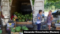 Жінки розмовляють біля фургона з кавунами, які виставлені на продаж на вулиці в Маріуполі, липень 2022 року