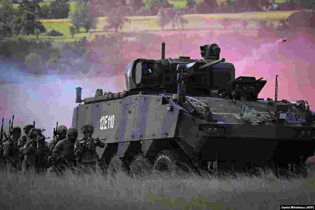 Militari francezi și români lângă un vehicul blindat care lansează grenade fumigene în zona de antrenament din Cincu, pe 20 septembrie. Baza din județul Brașov este folosită de mai multă vreme pentru exerciții NATO, dar lucrările de amenajare de acum vor permite ca circa 1.000 de soldați NATO și armament greu să se afle permanent aici. &nbsp;