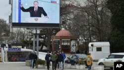 People in Sevastopol on the occupied Ukrainian peninsula of Crimea walk in front of a TV screen showing Russian President Vladimir Putin during his annual state of the nation address in February. 