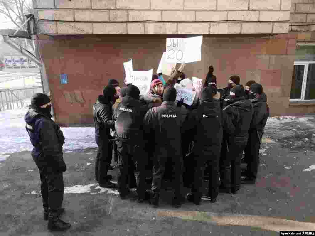 Полиция жасағы наразылыққа шыққан "Oyan, Qazaqstan" қозғалысының мүшелерін қоршап тұр. Қоршаудағы бірнеше адам "Парламенттік республика", "Сендер ұрысыңдар" (Вы - воры) деген сияқты плакаттар көтеріп тұр. Полицейлер саны наразы адамдардан әлдеқайда көп.&nbsp;