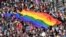 Oameni mărșăluiesc cu steagul curcubeu uriaș dinspre clădirea Parlamentului din centrul Budapestei în timpul paradei LGBT Pride pe 6 iulie 2019.