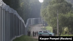 Grăniceri polonezi lângă zidul ridicat pentru a opri trecerile de migranți la granița cu Belarus, în apropiere de Kuznica, Polonia, 30 iunie 2022.