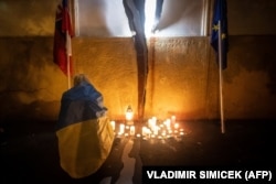 O femeie îmbrăcată într-un steag ucrainean aprinde o lumânare la un memorial pentru jurnaliștii de investigație uciși, Jan Kuciak și Martina Kusnirova, ca reacție la rezultatele alegerilor de la Bratislava din 1 octombrie.
