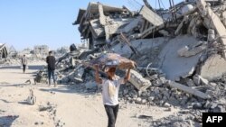 Un băiat palestinian cară bunuri personale pe lângă dărâmăturile clădirilor distruse în cartierul al-Tuffah din orașul Gaza, pe 27 octombrie 2025.