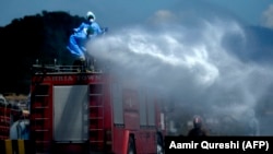Workers wearing protective gear spray disinfectant on a street at a residential area in Islamabad on March 29.