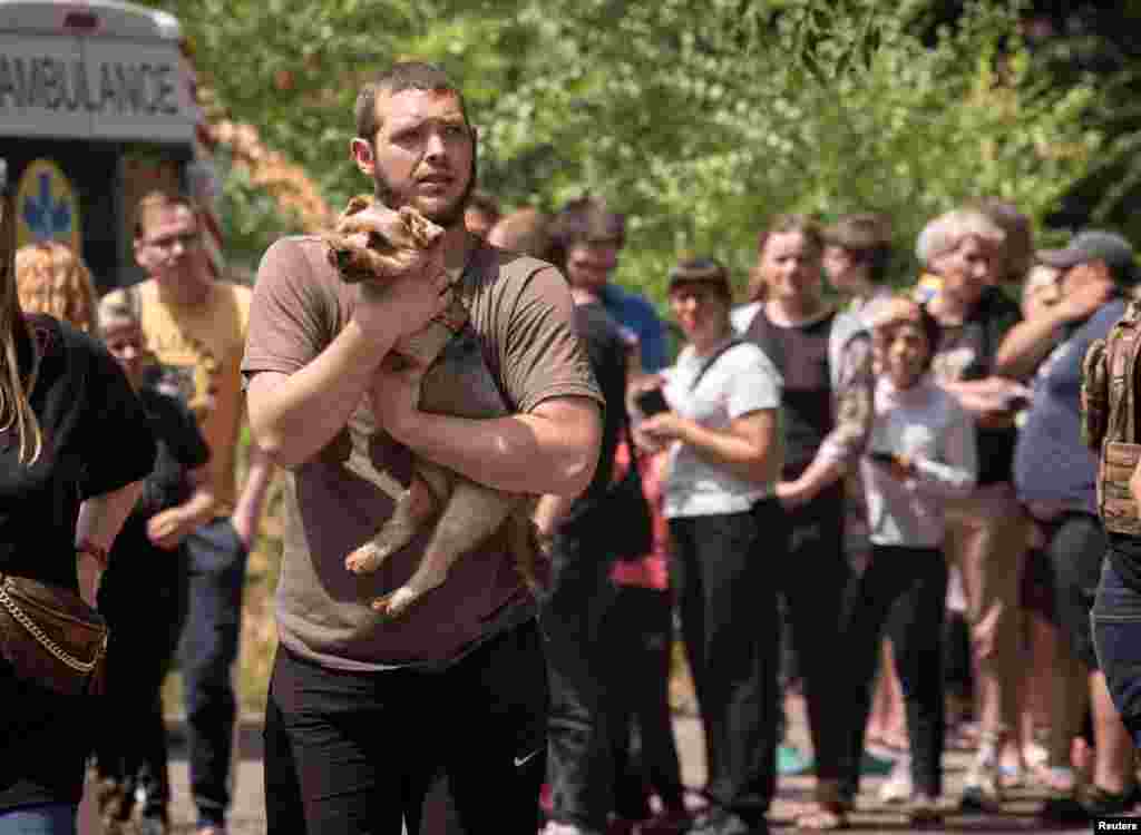 Украинанын чыгышындагы Днепр шаарында ит көтөрүп бараткан киши. Арттагы адамдар Орусиянын ракета чабуулунан жабыркаган көп кабаттуу үйдүн жанында топтолуп турушат.