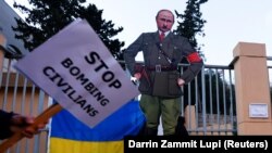 Картонна карикатура на президента Росії Володимира Путіна у вигляді Адольфа Гітлера біля посольства Росії в Республіці Мальта. На плакаті напис англійською: «Припиніть бомбардування мирних жителів». 8 березня 2022 року