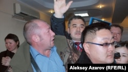 Неизвестный мужчина в синей рубашке не дает пройти к президиуму экоактивисту Абаю Ерекенову (в центре) на общественных слушаниях по строительству ГЛК "Кокжайляу". Алматы, 19 января 2015 года.