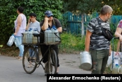 Люди стоять у черзі, щоб забрати воду, доставлену цистерною, в Донецьку, липень 2025 року