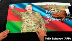 Адамдар Таулы Қарабақтағы соғыста жеңісті атап өту үшін көлігінің терезесіне Әзербайжан президенті Ильхам Әлиевтің портреті салынған  суретті жапсырып жатыр. Баку. 20 қараша, 2020 жыл. 