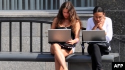 Teenage girls work on laptop computers while wating for a bus in Moscow
