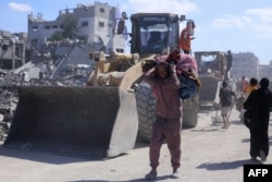 Buldozerele din Gaza trec pe lângă persoane strămutate, în drumul lor spre curățarea molozului de pe principalele axe și străzi din orașul Gaza, în contextul unui armistițiu între Israel și facțiunile palestiniene, pe 14 octombrie 2025.